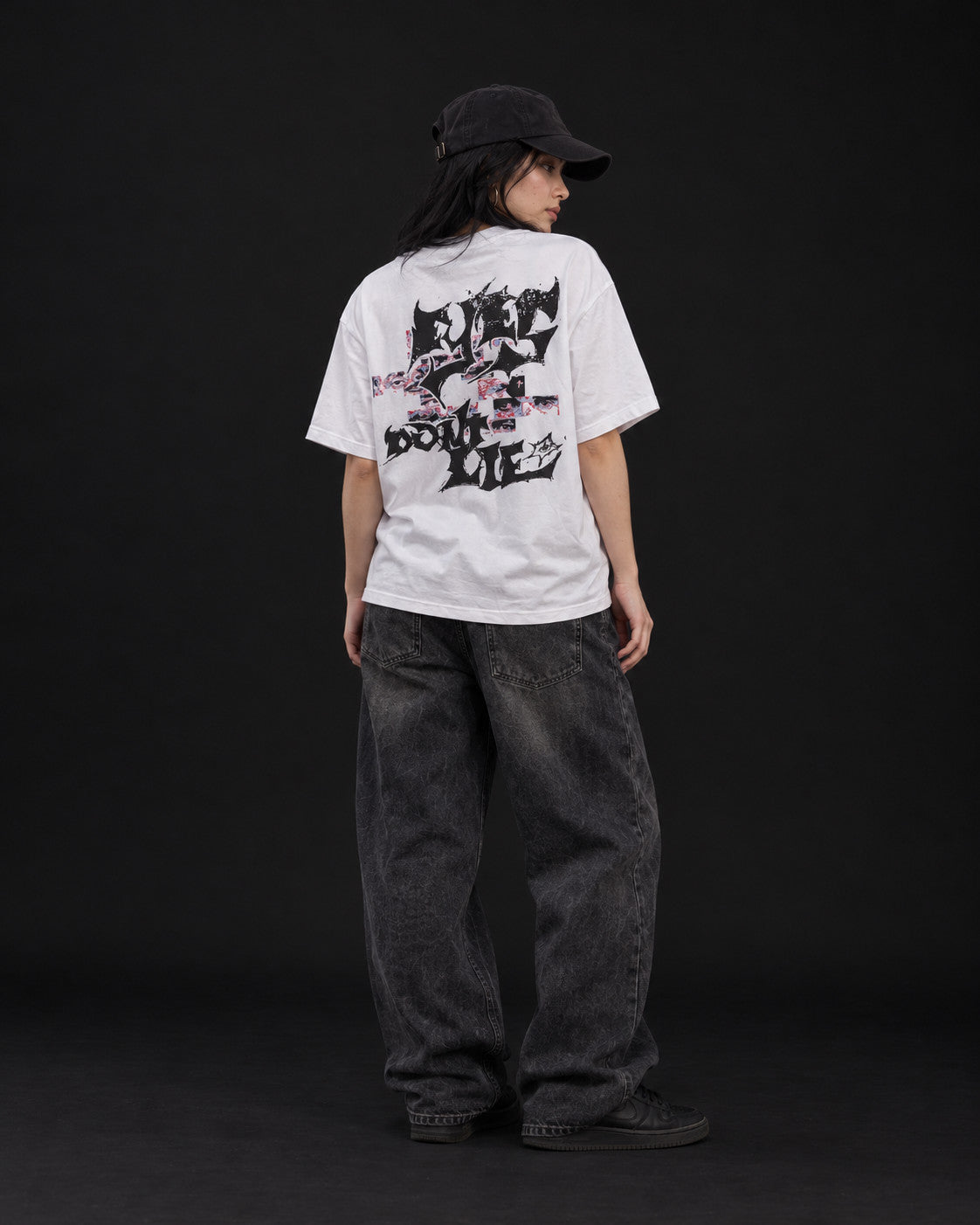 Back view of a model in the white VAGRANT IV Eyes Don't Lie T-shirt, showing the distressed lettering and eye-strip back print, studio shot